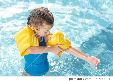 Cute little girl in swimwear putting on yellow inflatable safety sleeves on arms 71499004