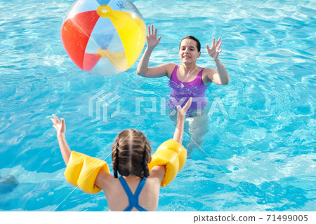 Young mother playing ball with her cute little daughter in transparent water 71499005