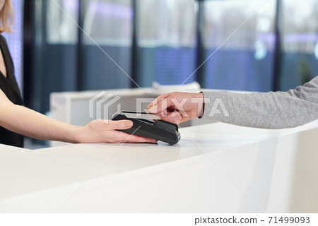 Young man holding smartphone over teminal held by female administrator Young man holding smartphone over teminal held by female administrator 71499093