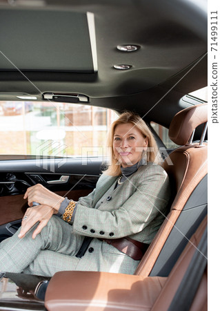 Pretty businesswoman looking at you with smile while sitting on backseat of car Pretty businesswoman looking at you with smile while sitting on backseat of car 71499111