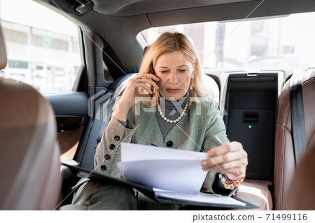 Mature businesswoman sitting on backseat of car and calling business partner 71499116