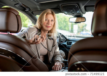 Happy mature female sitting in car and looking at you while going to drive Happy mature female sitting in car and looking at you while going to drive 71499121