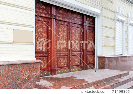 brown wooden entrance doors with a traditional hand-carved pattern with granite threshold and stone steps, side view. brown wooden entrance doors with a traditional hand-carved pattern with granite threshold and stone steps, side view. 71499505