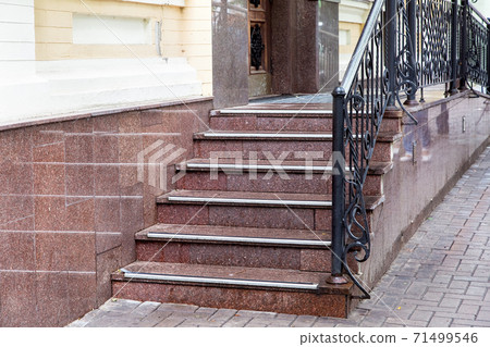 marble staircase with a rise to the front door with rubber non-slip stripes and black forged handrails, threshold with steps entrance close up. 71499546