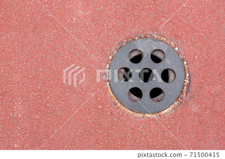 drainage hole with a round grid on a sports track made of red granular surface with copy space, top view close up. 71500415