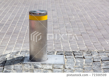 hydraulic gray electric bollard with a yellow reflective strip on the old stone tile road side view with copy space. hydraulic gray electric bollard with a yellow reflective strip on the old stone tile road side view with copy space. 71500509