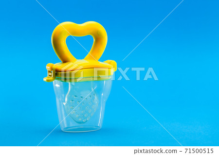 Fruit feeder in a plastic case with a yellow handle and a silicone pacifier on a blue background with a copy space. 71500515