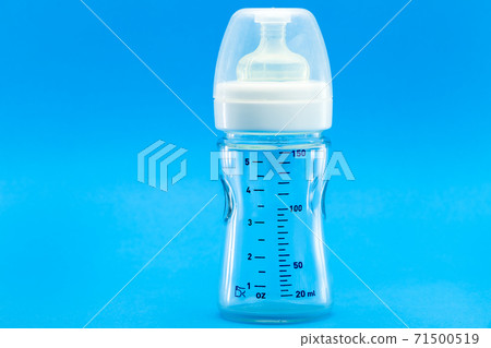 glass bottle with a measuring scale and a silicone pacifier for feeding babies, a transparent plastic cap isolated on a blue background with copy space. 71500519