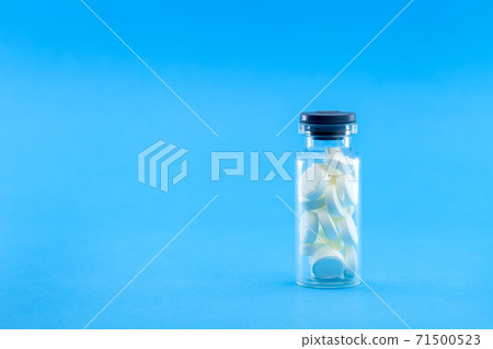 full glass bottle with white pills on a blue background, conceptual medical background with copy space. 71500523