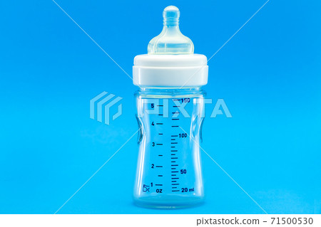 glass bottle with a measuring scale and a silicone pacifier for feeding babies, a transparent isolated on a blue background with copy space. glass bottle with a measuring scale and a silicone pacifier for feeding babies, a transparent isolated on a blue background with copy space. 71500530