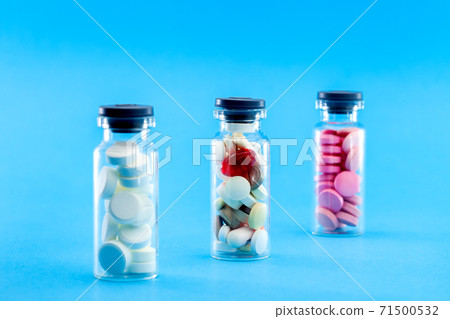 glass bottles filled with pills on a blue background, conceptual medical background. glass bottles filled with pills on a blue background, conceptual medical background. 71500532