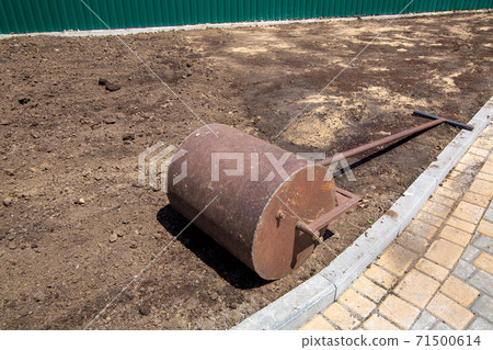 garden roller for compaction of the soil an iron shaft lies on the rolled ground on a sunny day, closeup of a landscape design process nobody. 71500614