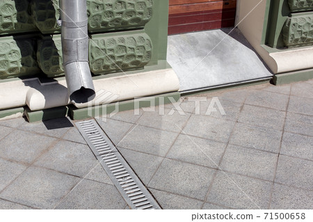 urban engineering structure downspout on green facade building with drainage grate of gray stone granite sidewalk from square tiles with copy space, closeup details city infrastructure, nobody. 71500658