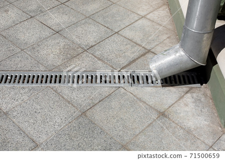an engineering city improvement a downspout with a drainage grate against a background of a gray stone granite sidewalk from square tiles, side view closeup nobody. 71500659