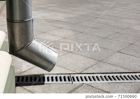 street engineering structure a downspout pipe with drainage gutter on a background of a gray stone granite sidewalk from square tiles with copy space, side view closeup nobody. 71500660