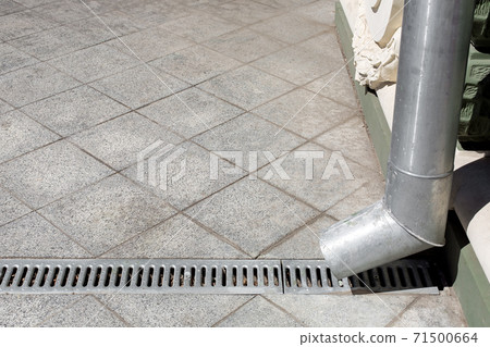 an engineering structure a downspout with a drainage grate against a background of a gray stone granite sidewalk from square tiles with copy space, side view closeup nobody. an engineering structure a downspout with a drainage grate against a background of a gray stone granite sidewalk from square tiles with copy space, side view closeup nobody. 71500664