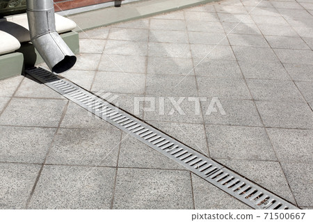 galvanized downspout on facade building with iron drainage grate of gray stone granite sidewalk from square tiles on ground, closeup details city infrastructure, nobody. galvanized downspout on facade building with iron drainage grate of gray stone granite sidewalk from square tiles on ground, closeup details city infrastructure, nobody. 71500667