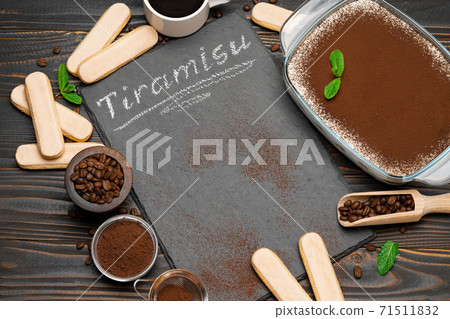 Traditional Italian Tiramisu dessert in glass baking dish, cup of coffee and savoiardi cookies on stone serving board with chalk inscription sign on wooden background 71511832