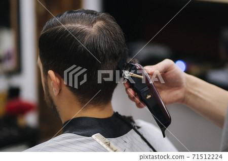 Back view of Men in beauty salon. Men's haircut in a barbershop. New haircut style 2021. Professional hairdresser uses a hair clipper for fringing hair Back view of Men in beauty salon. Men's haircut in a barbershop. New haircut style 2021. Professional hairdresser uses a hair clipper for fringing hair 71512224