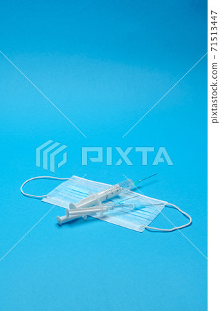 Syringe and disposable face mask to prevent COVID-19 virus on blue background Syringe and disposable face mask to prevent COVID-19 virus on blue background 71513447