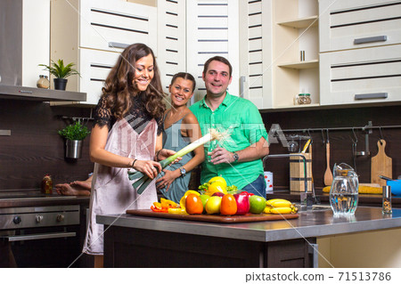 Happy couple looking to cooking woman in kitchen Happy couple looking to cooking woman in kitchen 71513786