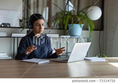Confident Indian businesswoman wearing headphones using laptop, speaking 71514710