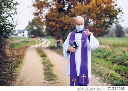 Catholic priest with a bible in a medical mask points with his finger Catholic priest with a bible in a medical mask points with his finger 71519002