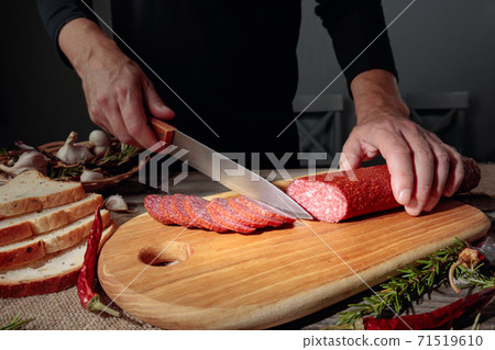Man cuts a sausage for a sandwich. Man cuts a sausage for a sandwich. 71519610