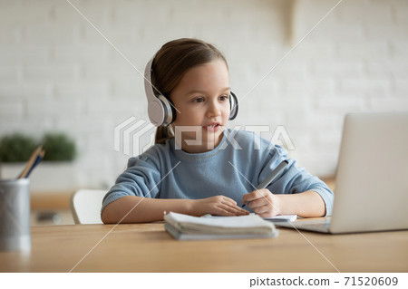 Focused little girl wearing headphones looking at laptop screen Focused little girl wearing headphones looking at laptop screen 71520609