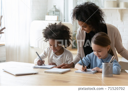 Smiling African American woman helping two little daughters with homework Smiling African American woman helping two little daughters with homework 71520702