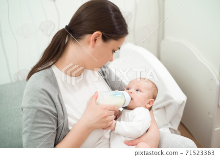 Woman holding a newborn baby in her arms and feeds him from a milk bottle. Woman holding a newborn baby in her arms and feeds him from a milk bottle. 71523363