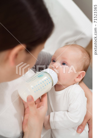 Woman holding a newborn baby in her arms and feeds him from a milk bottle. Woman holding a newborn baby in her arms and feeds him from a milk bottle. 71523365