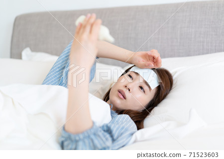 Young woman taking a fever and taking a temperature in bed 71523603