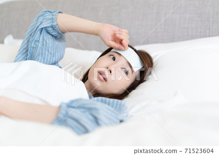A young woman who has a fever and cools her forehead in bed 71523604
