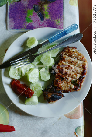 roasted steak meat with bone, cucumber , ketchup fork and knife 71523778