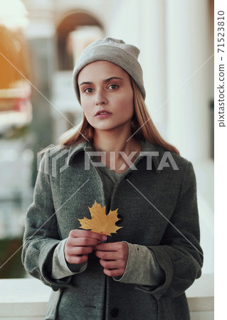 blond girl in knitted hat and coat with maple leaf close up portrait on city architecture background 71523810