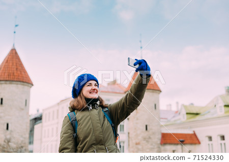 Tallinn, Estonia. Young Caucasian Girl Woman Backpacker Tourist Enjoying Life, Smiling, Having Fun And Taking Selfie Photo On Smartphone Near Landmark Viru Gate. Vacation In Old Town 71524330