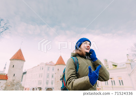 Tallinn, Estonia. Young Caucasian Woman Backpacker Tourist Enjoying Life, Smiling And Calling On Smartphone Near Landmark Viru Gate. Vacation In Old Town. Girl Surfing Net Internet In Phone 71524336