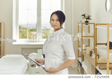 Serious professional beautician standing in her beauty salon and looking at camera Serious professional beautician standing in her beauty salon and looking at camera 71524409