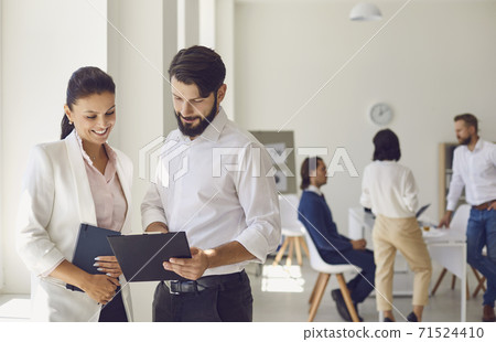 Cheerful female coworker giving advice to male colleague in modern office workspace Cheerful female coworker giving advice to male colleague in modern office workspace 71524410