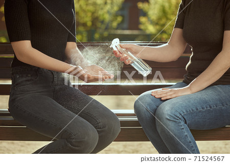 Women's hands are treated with a sanitizer girl's hands against the background of a bench. Outdoor photo. 71524567