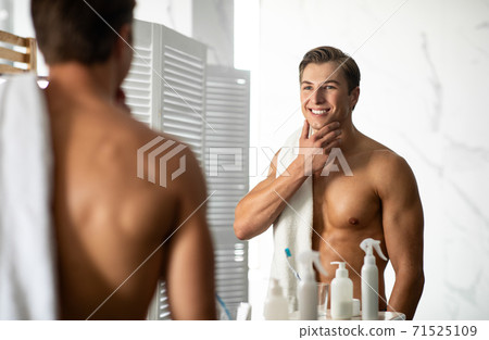 Confident young man looking in the mirror, touching chin Confident young man looking in the mirror, touching chin 71525109