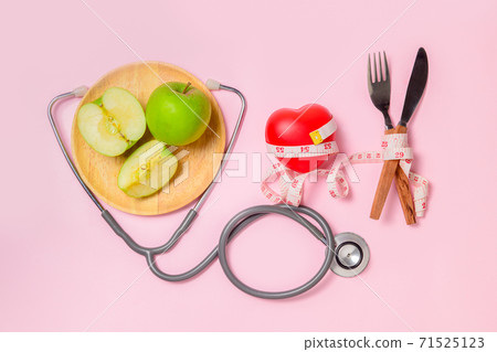Green apple on dish with stethoscope and measuring tape around fork and knife 71525123