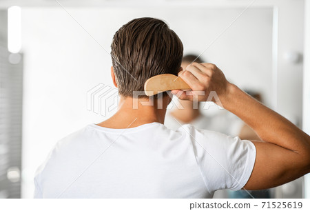 Young man looking in the mirror brushing hair Young man looking in the mirror brushing hair 71525619