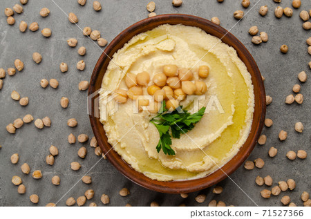 Flat lay view at hummus topped with green coriander leaves on stone table covered with chickpeas 71527366