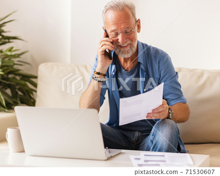 Cheerful aged freelancer making call in home office. Cheerful aged freelancer making call in home office. 71530607