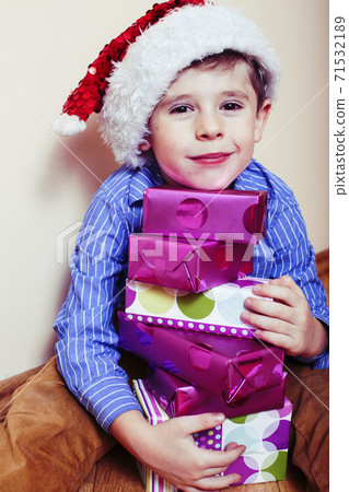 little cute boy with Christmas gifts at home wearing red Santas hat. closeup emotional happy smiling in mess with toys, lifestyle holiday people concept 71532189