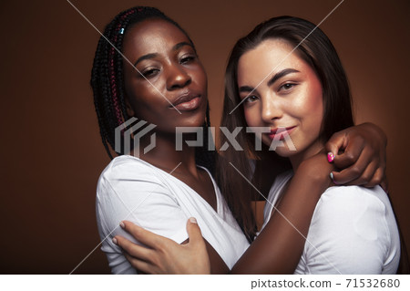 young pretty caucasian, afro woman posing cheerful together on brown background, lifestyle diverse nationality people concept young pretty caucasian, afro woman posing cheerful together on brown background, lifestyle diverse nationality people concept 71532680