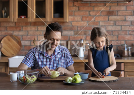 Caring father and little daughter cutting fresh vegetables at kitchen 71534424