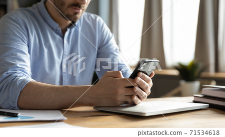 Closeup view businessman sit at desk holding smartphone texting message Closeup view businessman sit at desk holding smartphone texting message 71534618